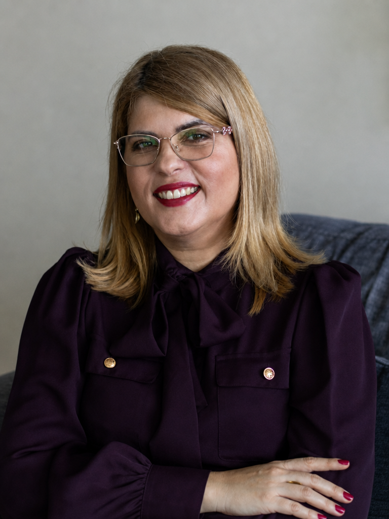 Adenir Landim sorrindo, usando uma blusa ameixa e óculos